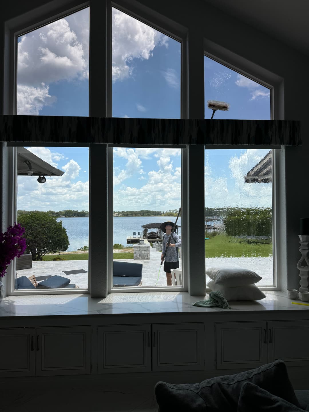 View of a lake through large windows, featuring a person cleaning the glass with a squeegee.
