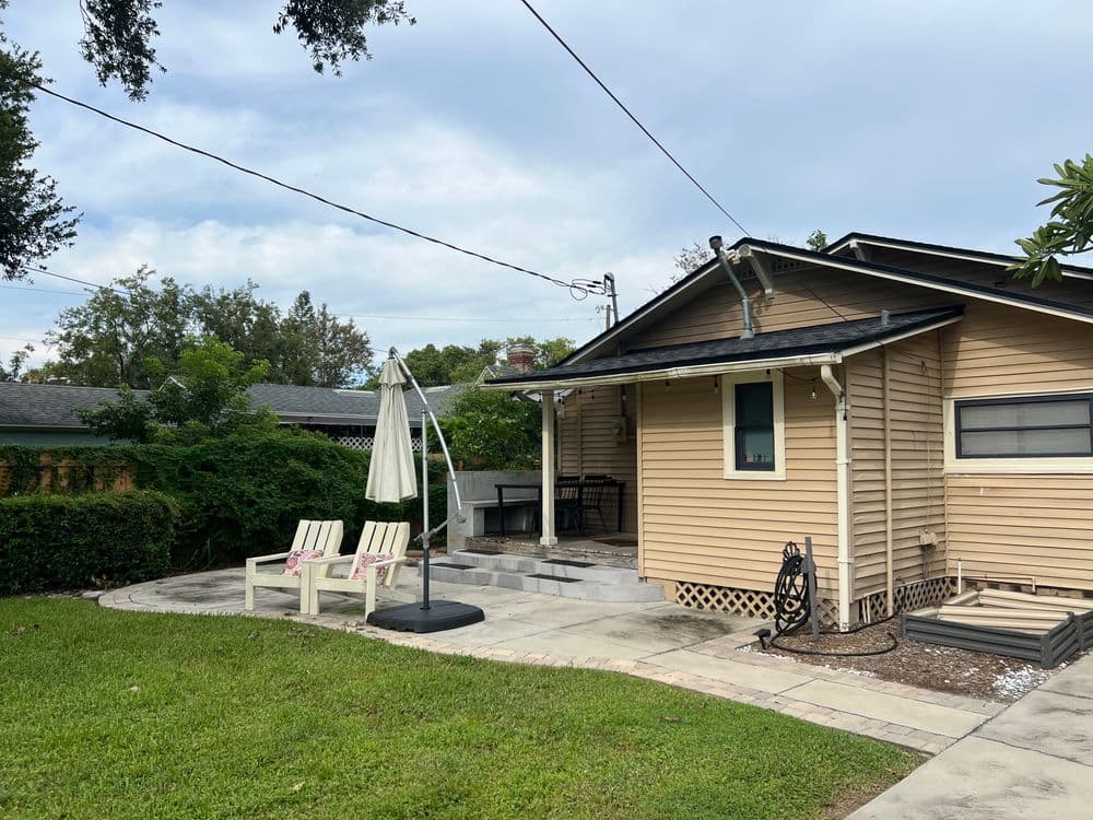 Cozy backyard with a patio, lounge chairs, and a shaded umbrella beside a charming home.