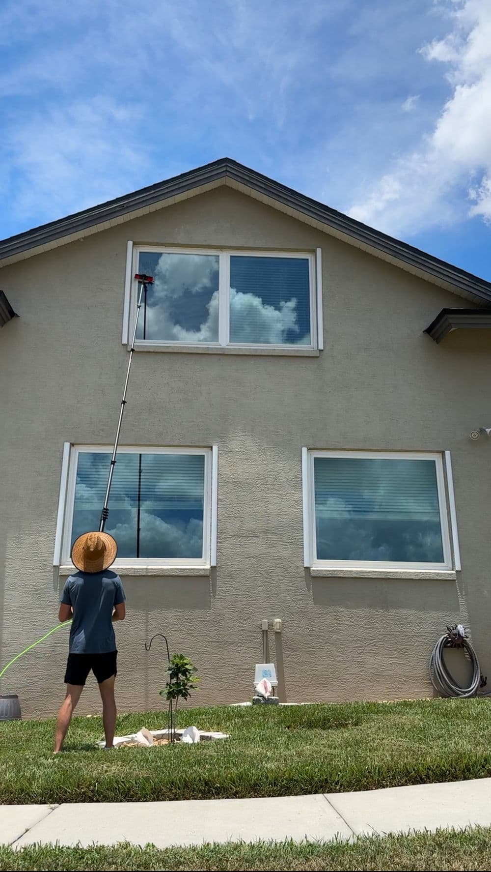 Person using a extendable pole to clean windows on a house with blue sky and clouds.