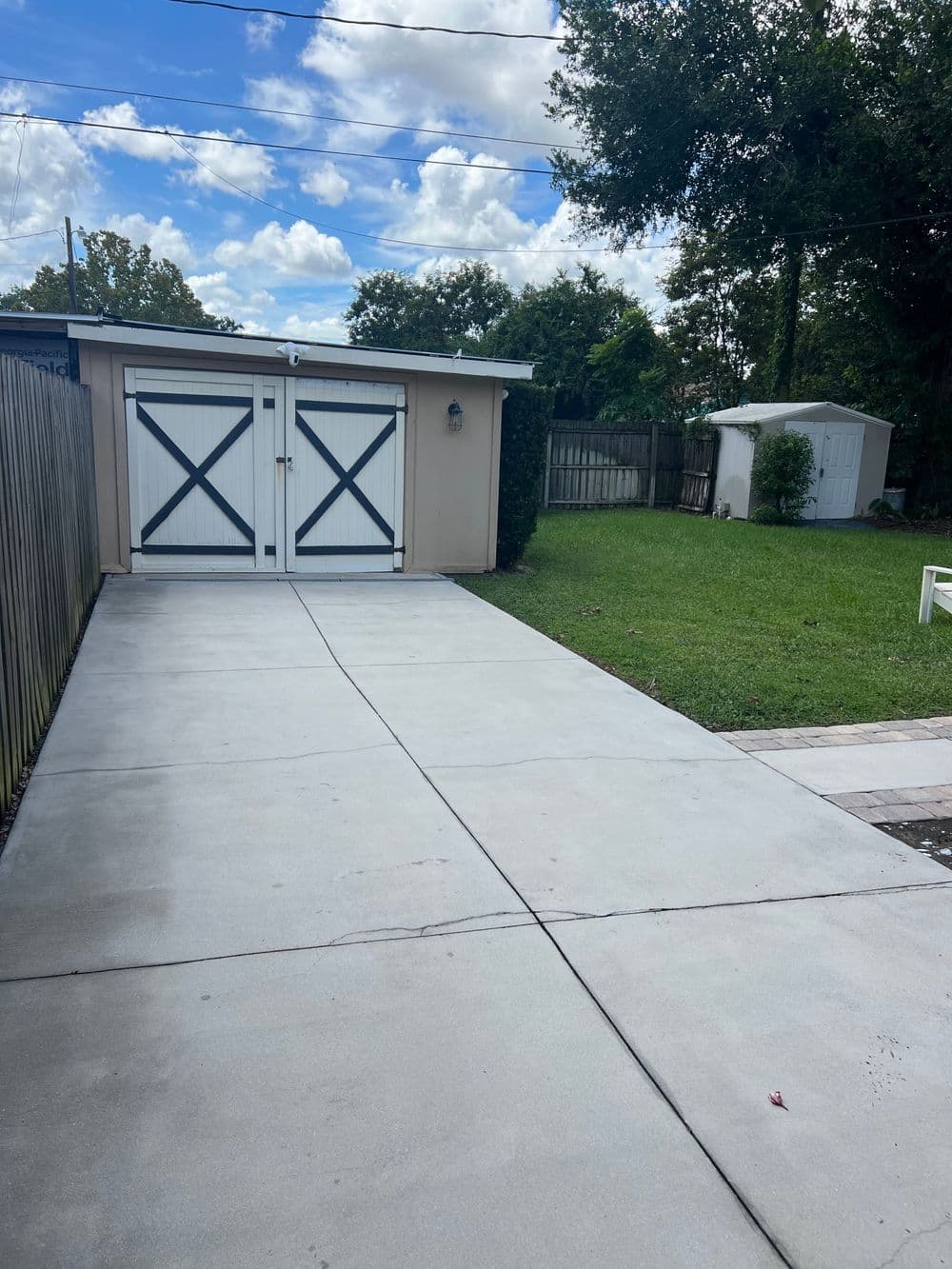 Driveway leading to a garage with white doors, surrounded by greenery and blue sky.