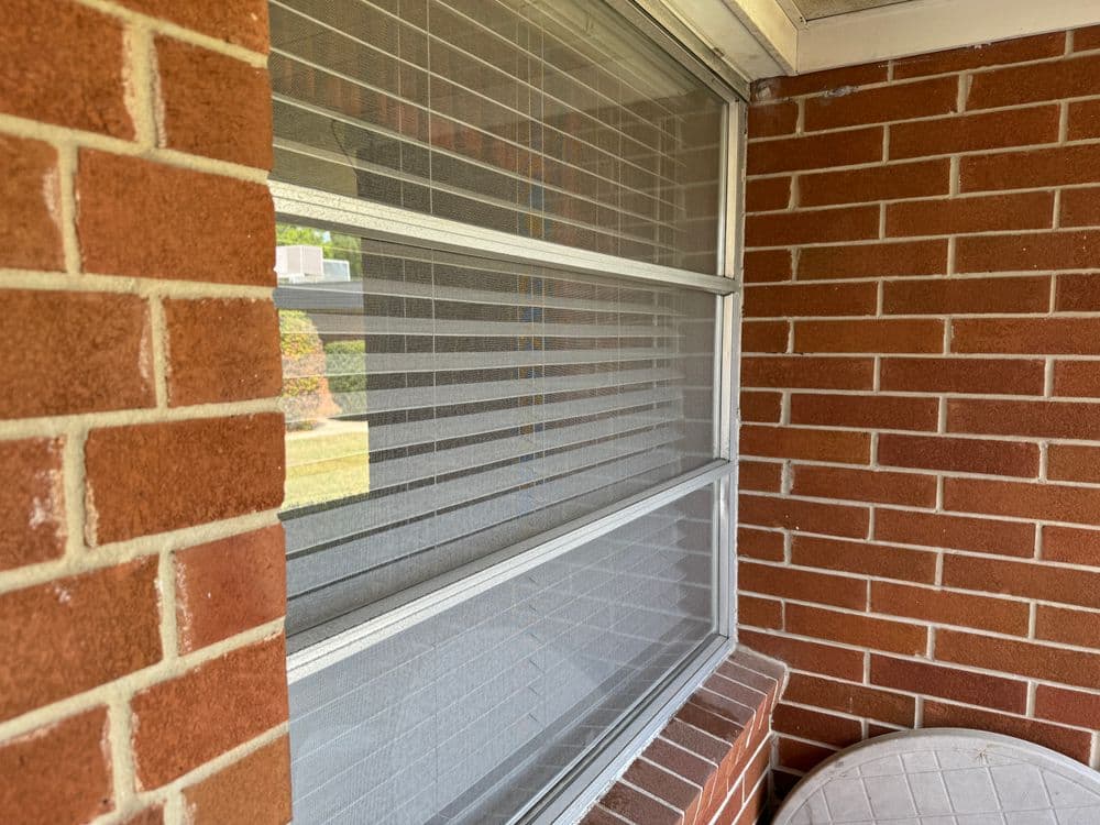 Exterior view of a window with blinds set into a brick wall, showcasing architectural details.