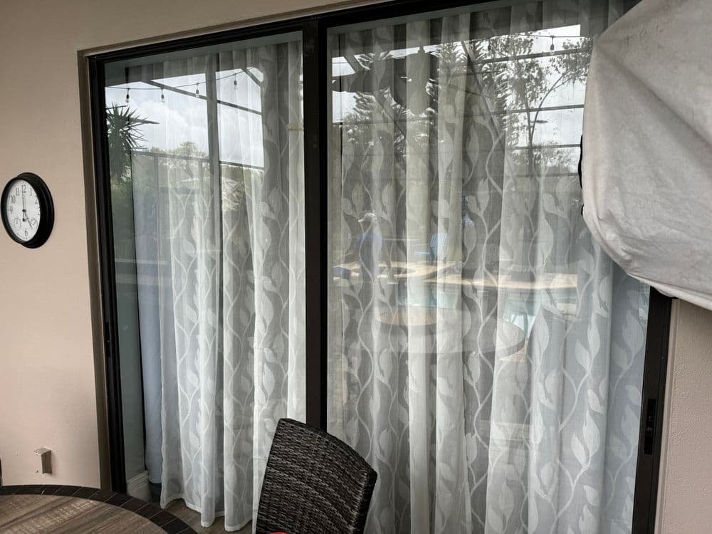 Sliding glass door with sheer curtains and outdoor view of a pool area.