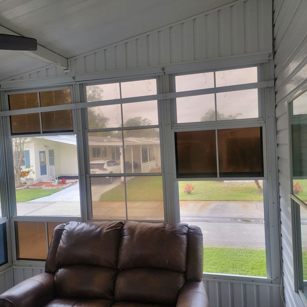 Cozy screened-in porch with leather sofa, showing a view of the driveway and neighborhood outside.
