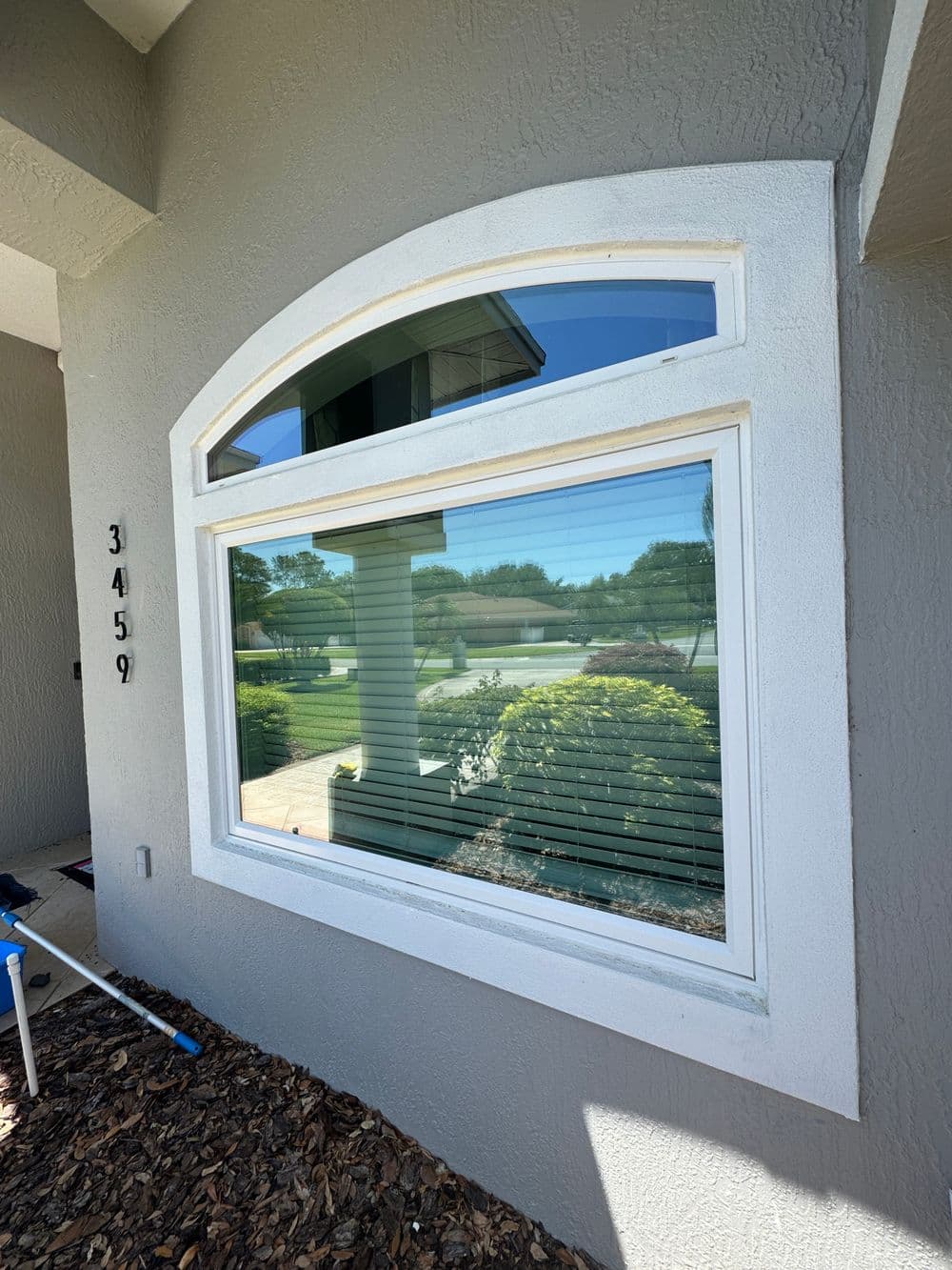 Arched window with blinds overlooking landscaped yard and path, contemporary home exterior.