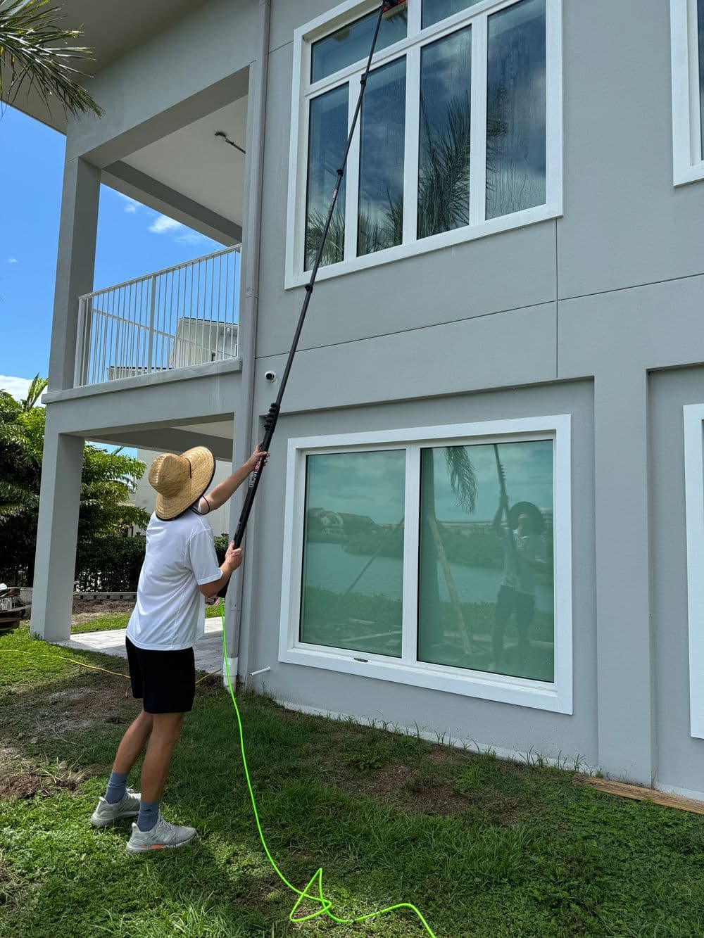 Person using a long pole to clean windows of a modern house on a sunny day.