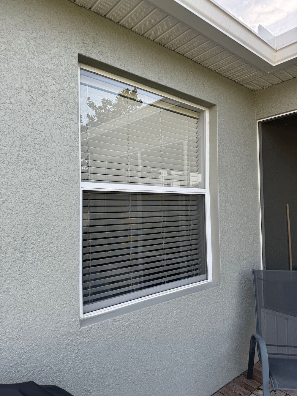Exterior view of a house window with blinds, featuring light-colored textured wall.