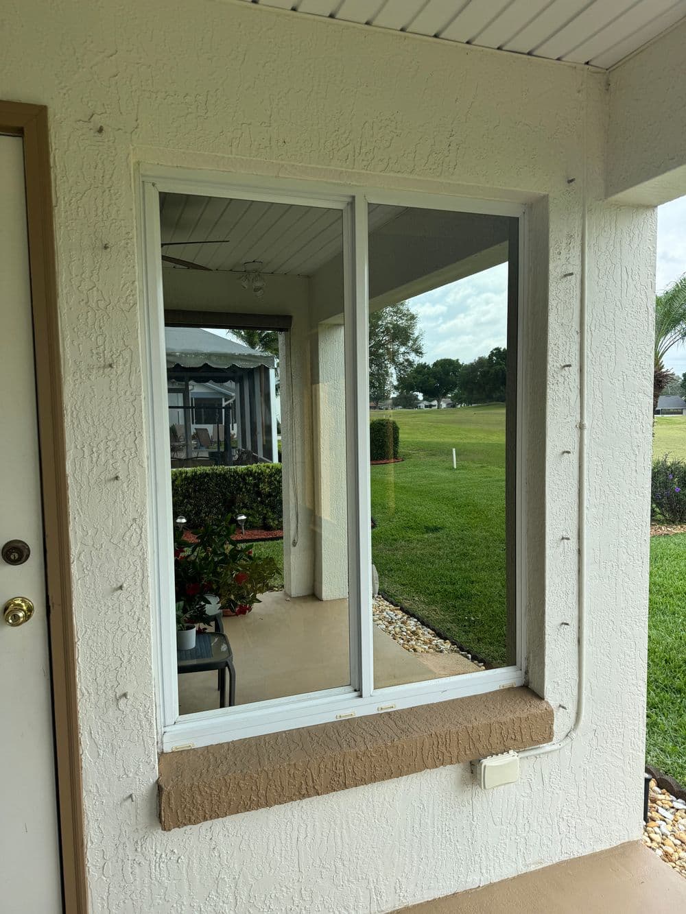 Modern window in a residential exterior, overlooking green lawn and garden area.