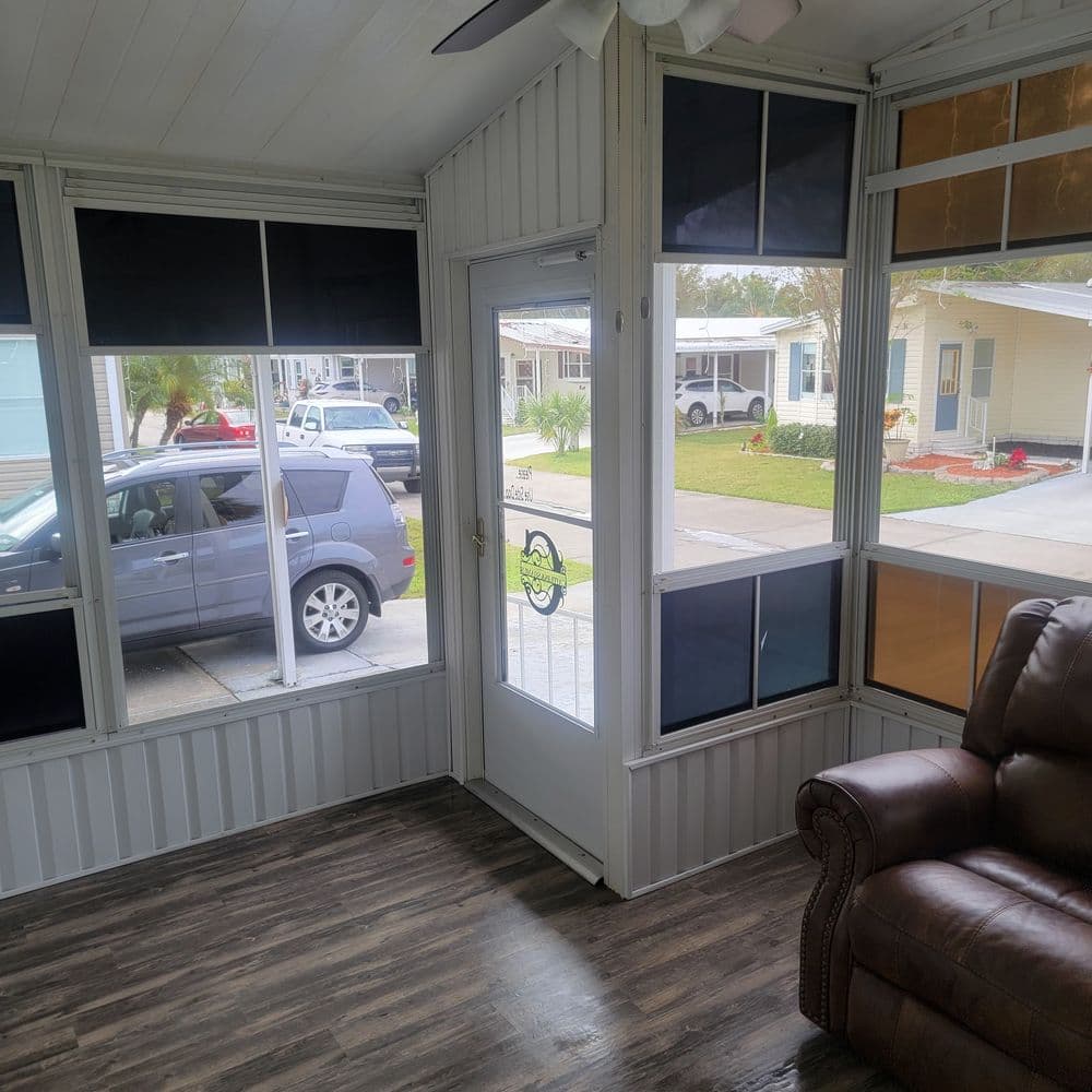 Sunny screened porch with comfortable brown chair, door to outside, and modern decor.