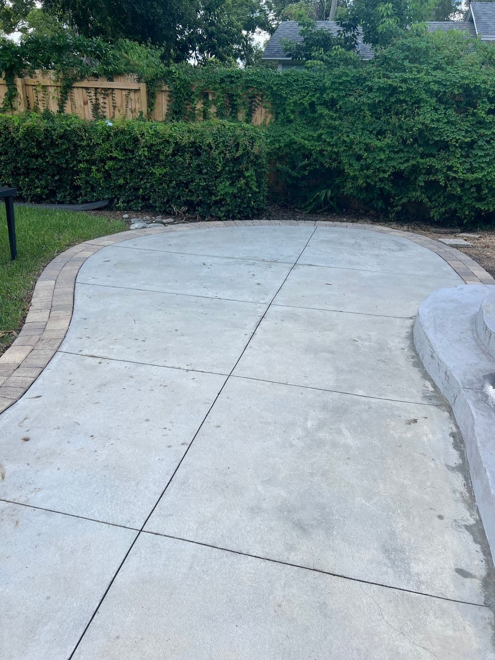 Curved concrete pathway leading to a landscaped area with greenery and a stone border.
